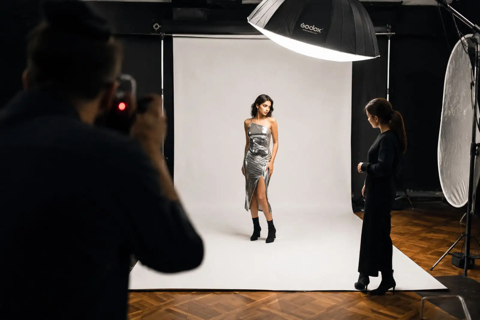A working set in the Brivon kochi studio — two stylists pinning a garment on a model while a photographer reviews tethered captures on a calibrated monitor.